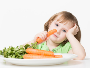 Ein Mädchen vor einem Bündel Karotten isst eine Karotte