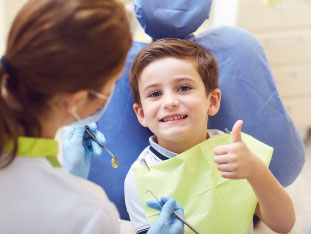 Ein fröhlicher Junge im Zahnarztstuhl zeigt während der Behandlung den Daumen hoch, alles OK!