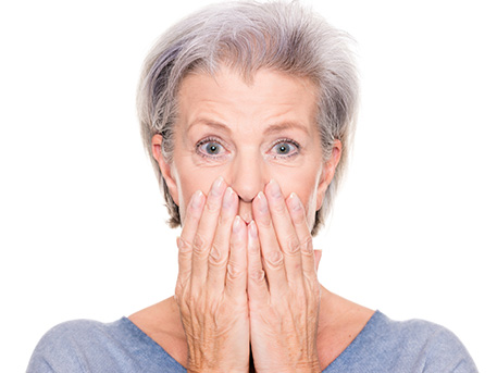 Ältere Frau verdeckt mit Händen schlecht sitzende Zahnprothese