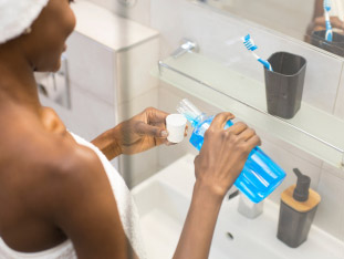 Eine Frau vor dem Spiegel im Badezimmer gießt sich Mundspülung in ein Glas