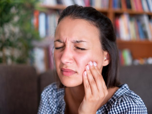 Eine junge Frau mit schmerzverzerrtem Gesicht hält sich vor lauter Zahnschmerz ihre Wange