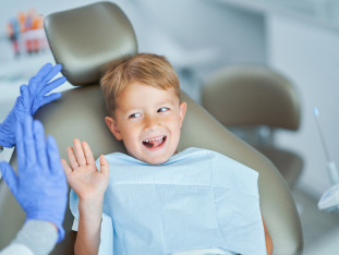 Ein kleiner Junge lacht und hat Spaß auf dem Zahnarztstuhl, er klatscht sich mit dem Zahnarzt ab