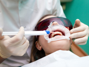 Im Behandlungsstuhl werden einer Patientin gerade mit Gel die Zähne gebleacht