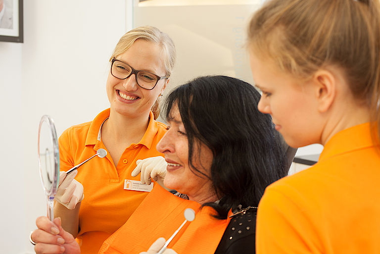 Patientin betrachtet ihre Zähne im Spiegel in Anwesenheit des Teams der Zahnklinik Düsseldorf